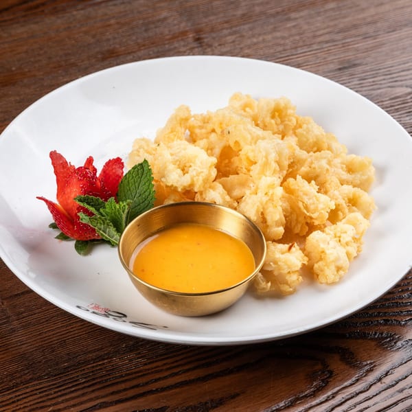 Crispy fried calamari with a side of orange dipping sauce, garnished with strawberry and mint.