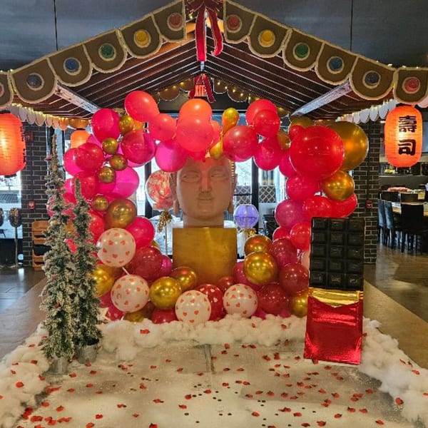 A festive Sogo Hibachi and Sushi Lounge entrance with red and gold balloons, a Buddha statue, and a chocolate bar.