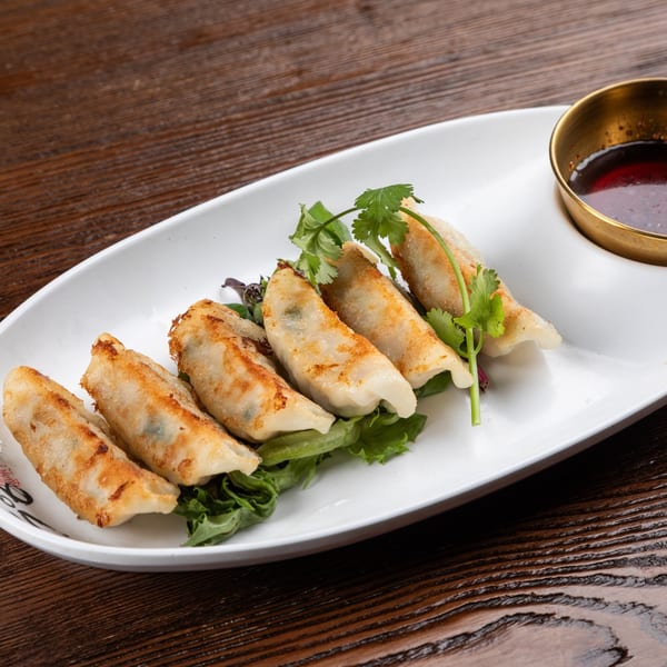Six pan-fried Japanese gyoza dumplings on lettuce with cilantro and a side of dipping sauce.