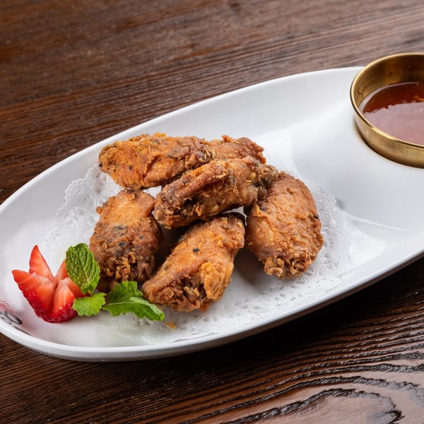 Crispy fried chicken wings with sliced strawberries, mint, and a dipping sauce on a white plate.