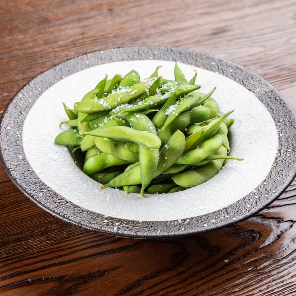 A white and black bowl filled with bright green edamame pods, sprinkled with sea salt.