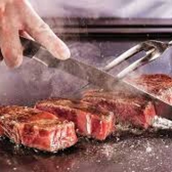 Chef's hands slicing sizzling hibachi steak on a grill at Sogo Hibachi and Sushi Lounge.