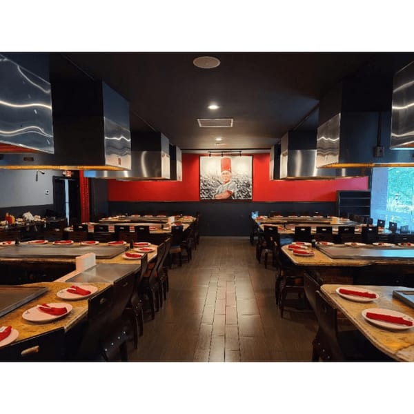 Sogo Hibachi and Sushi Lounge dining room with hibachi tables, red accents, and a chef portrait.