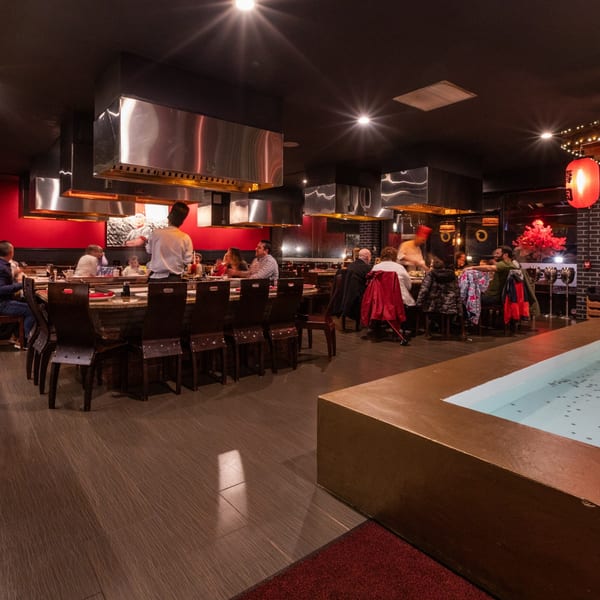 Diners seated around hibachi grills with chefs cooking at Sogo Hibachi and Sushi Lounge.