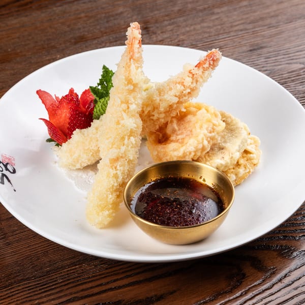 Crispy shrimp and vegetable tempura with a dark dipping sauce, garnished with strawberries and mint.