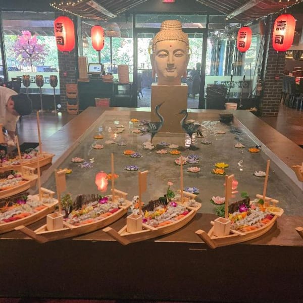 Sushi boats float on a water feature with a large Buddha head statue in the background at Sogo Hibachi.