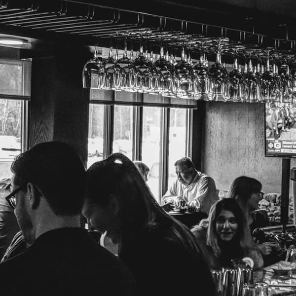 Black and white image of Sogo Hibachi and Sushi Lounge bar with hanging glasses and patrons.